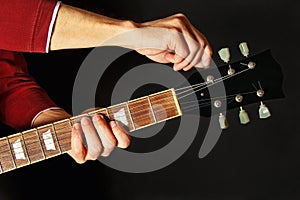 Hands tunes the electric guitar on dark background