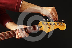 Hands tunes the guitar on black background