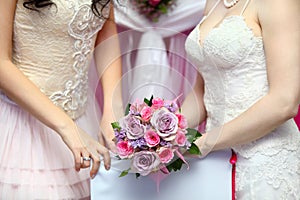 Hands of two brides wearing dresses hold bouquet