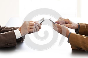 Hands from two businessmen in conversation by a desk. Both men is texting on a cell phones. Negotiating business or a job intervie