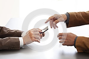 Hands from two businessmen in conversation by a desk. One texting on a cell phone and the other pointing. Negotiating business or