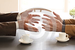Hands from two businessmen in conversation by a desk. Two cups of coffee on the table. Negotiating business or a job interview. -
