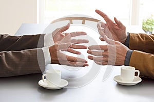 Hands from two businessmen in conversation by a desk. Two cups of coffee on the table. Negotiating business or a job interview. -
