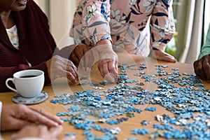 Hands of two diverse senior women and african american male friend doing puzzles