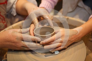 Hands of two people create pot on potter's wheel photo