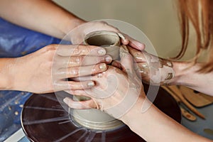 Hands of two people create pot, potter`s wheel. Teaching pottery