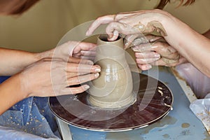 Hands of two people create pot, potter`s wheel. Teaching pottery photo