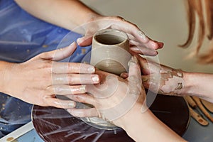 Hands of two people create pot, potter`s wheel. Teaching pottery photo
