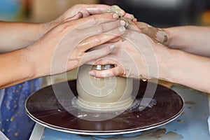 Hands of two people create pot, potter`s wheel. Teaching pottery photo