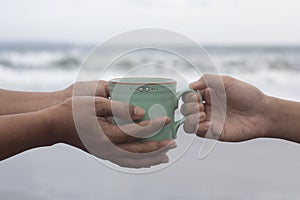 Hands of two people holding a cup of coffee or tea on beach background. Take and give or giving and receive concepts.