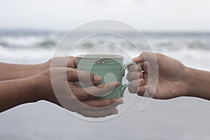 Hands of two people holding a cup of coffee or tea on beach background. Take and give or giving and receive concepts. photo