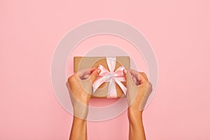 Hands tying a bow on present box on pink flatlay