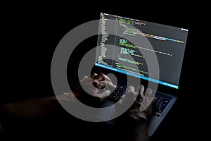 Hands typing code on a laptop screen in a dark room, programmer at work
