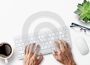 Hands typing on computer keyboard over white office desk table with cup of coffee and supplies