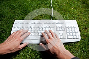 Hands typing keyboard on the grass