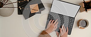 Hands typing keyboard tablet on white table with notebook, notepad, pencils and vase