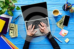 hands typing on laptop keyboard on blue wooden table with stationery and money