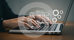 Hands typing on a laptop keyboard, with digital icons overlayed, including a magnifying glass, document, check marks, and gears ge photo