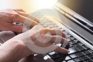 Hands typing on a laptop keyboard, light effect