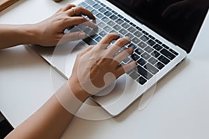 Hands typing on a laptop keyboard for work or study on a clean white desk in a bright office space