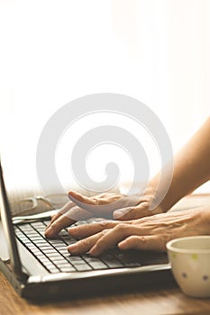 Hands typing laptop on table with coffee mug