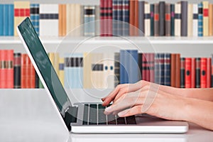 Hands typing on notebook in library