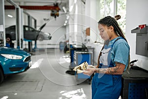 Hands that understand automobile. Young african american woman, professional female mechanic looking down, wiping