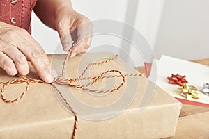 Hands of an unknown mature woman tying a Christmas gift with a decorative string