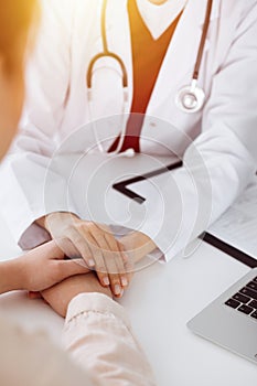 Hands of unknown woman-doctor reassuring her female patient in sunny room, close-up