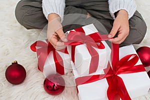 Hands unraping gift boxes with red ribbon and christmas ball. Child with Christmas present, banner copy space. Top view