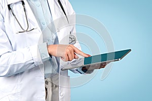 Hands of unrecognizable woman doctor in white coat working on digital tablet, closeup