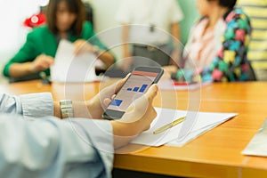 Hands using cell phone with stock money graph with group of business people.