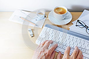 Hands using a computer keyboard on an office desk with coffee, usb stick and papers, business at home concept, copy space,