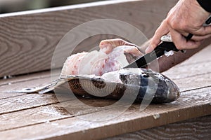 Hands Using Knife To Filet A Fish To Eat