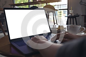 Hands using laptop with blank white desktop screen with coffee cup and cake on wooden table in cafe