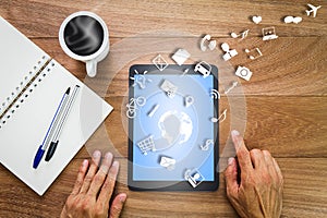 Hands using tablet computer with world map, social and business icons, notebook,pens and hot coffee cup on wooden desk