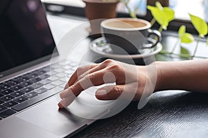 Hands using and touching on laptop touchpad with coffee cup on wooden table