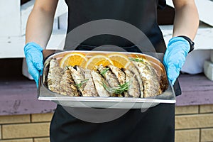In the hands of the waitress holds dishes with baked fish.