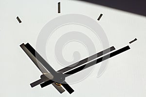 Hands of a wall clock, with shadows on white, cementitious background structure. shadow in upper part of picture