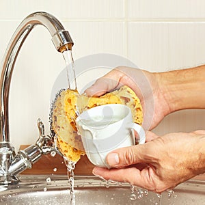 Hands wash the cup under running water in kitchen