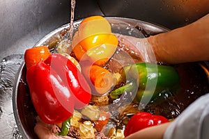 Hands wash vegetables in basin.