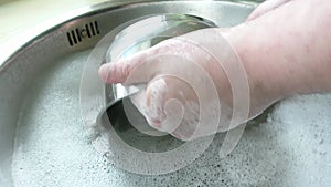 Hands washing dishes in metal sink with soap bubbles