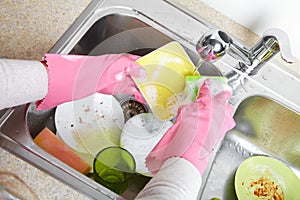 Hands washing dishes with running water from faucet