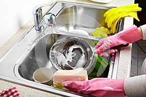 Hands washing dishes with running water from faucet