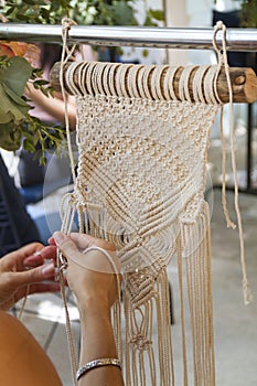 Hands weaving macrame tapestry with beige thread photo