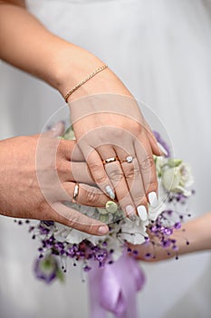 hands with wedding rings over a bouquet of flowers in shallow depth of field