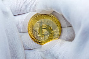 Hands with white gloves holding a golden bitcoin