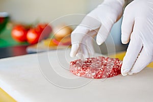 Hands in white gloves prearing a fresh hamburger patty