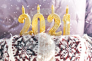 Hands in winter mittens are holding the numbers 2021 gold on a lilac background, it is snowing, happy new year 2021