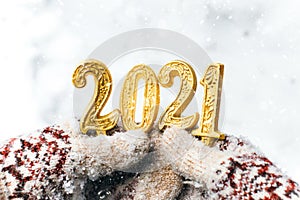 hands in winter mittens are holding the numbers 2021 gold on a white background